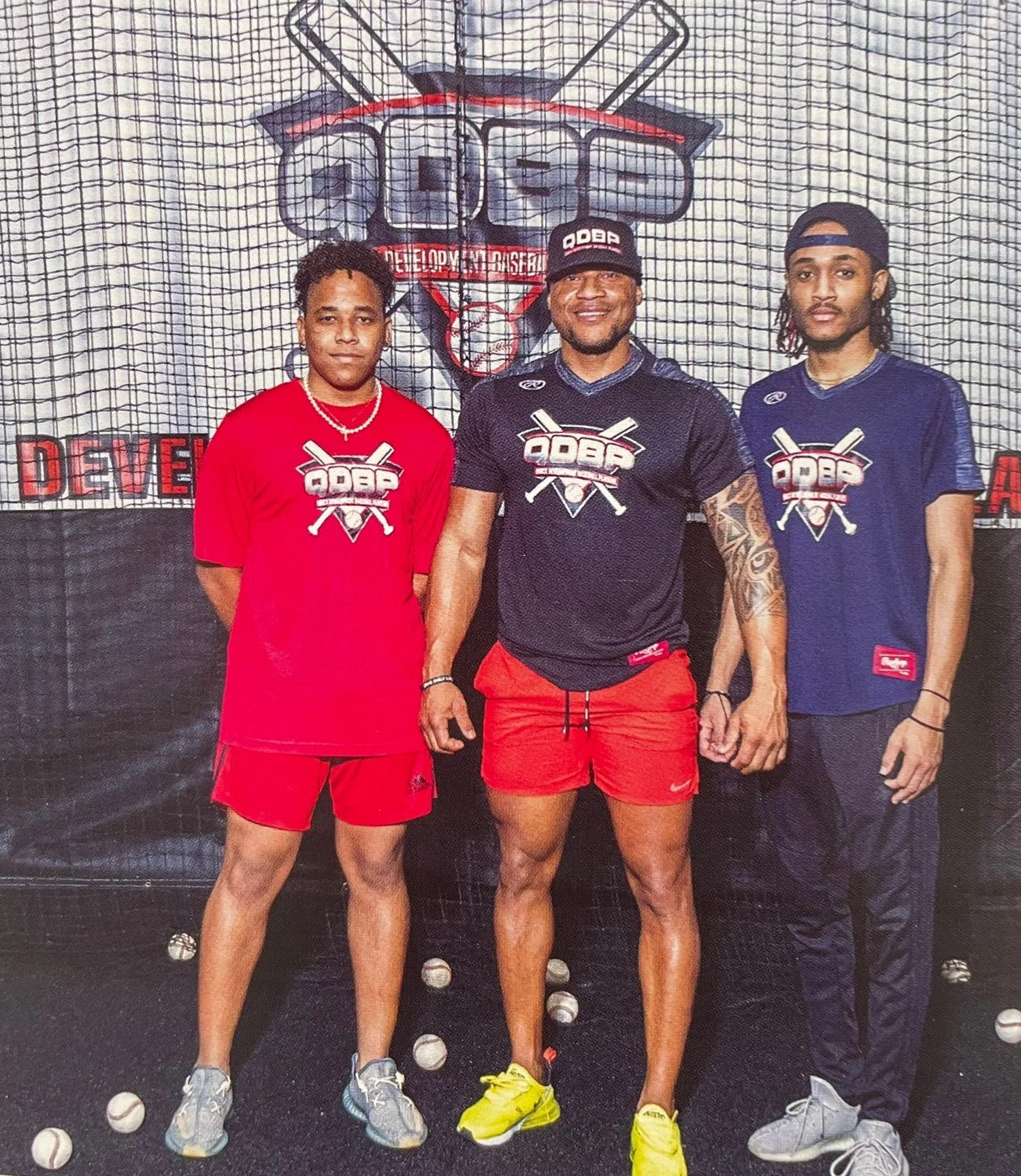 Three people in QDBP apparel standing together in front of the QDBP logo